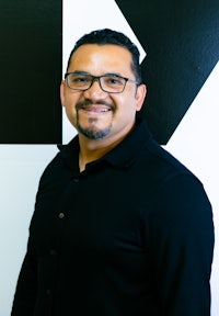 a man in glasses smiling in front of a black and white sign